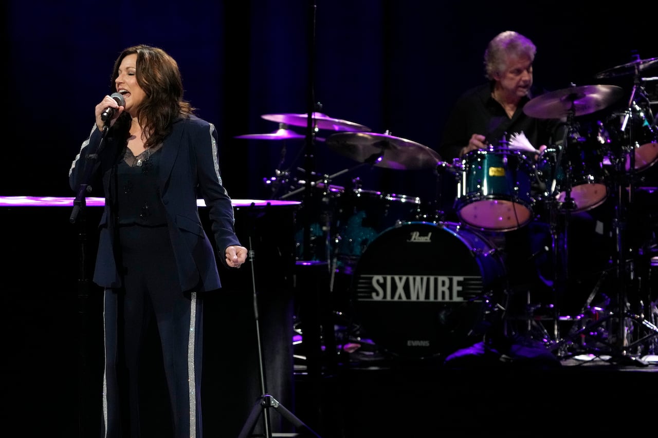 একজন মহিলা স্টেজে মাইক্রোফোনে গান গাইছেন।