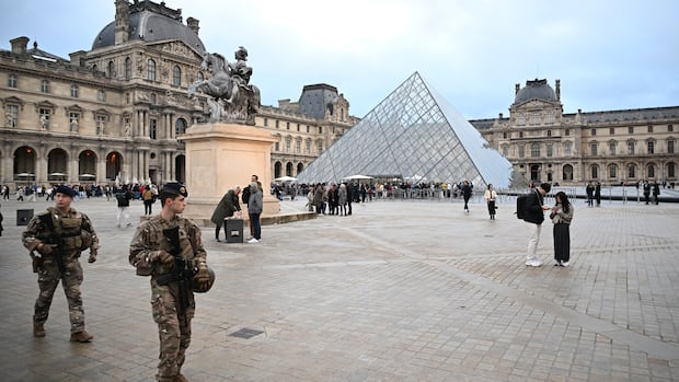 Soldiers stand near a glass pyramid in a busy square