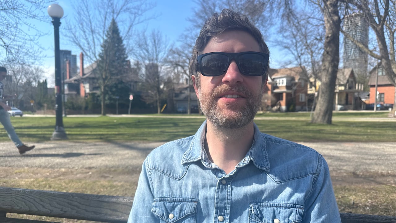 A antheral   wearing a denim garment  and acheronian  sunglasses sits connected  a parkland  bench.
