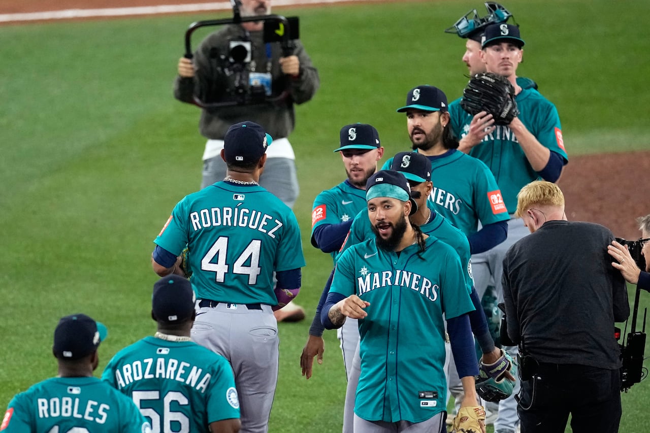 A group of baseball players celebrate a victory on a baseball field, following the end of the game
