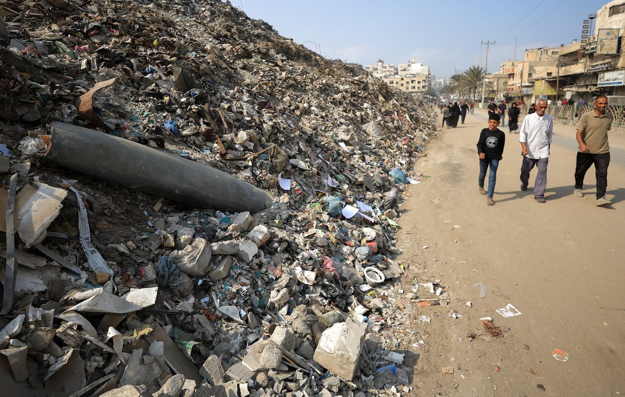 People walk past huge piles of rubbish in Gaza, including remains of a kind