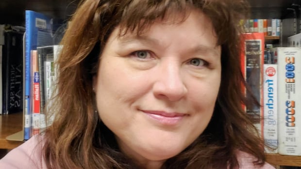 A woman with long brown hair smiles in front of a bookshelf. 
