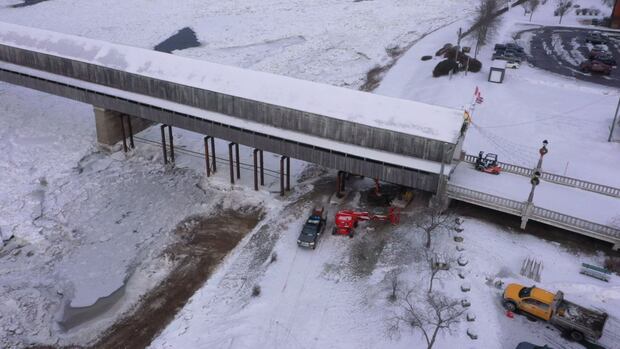 The Hartland covered bridge is closed during construction A drone shot of cranes and construction equipment being used underneath a large, snow-covered, covered bridge