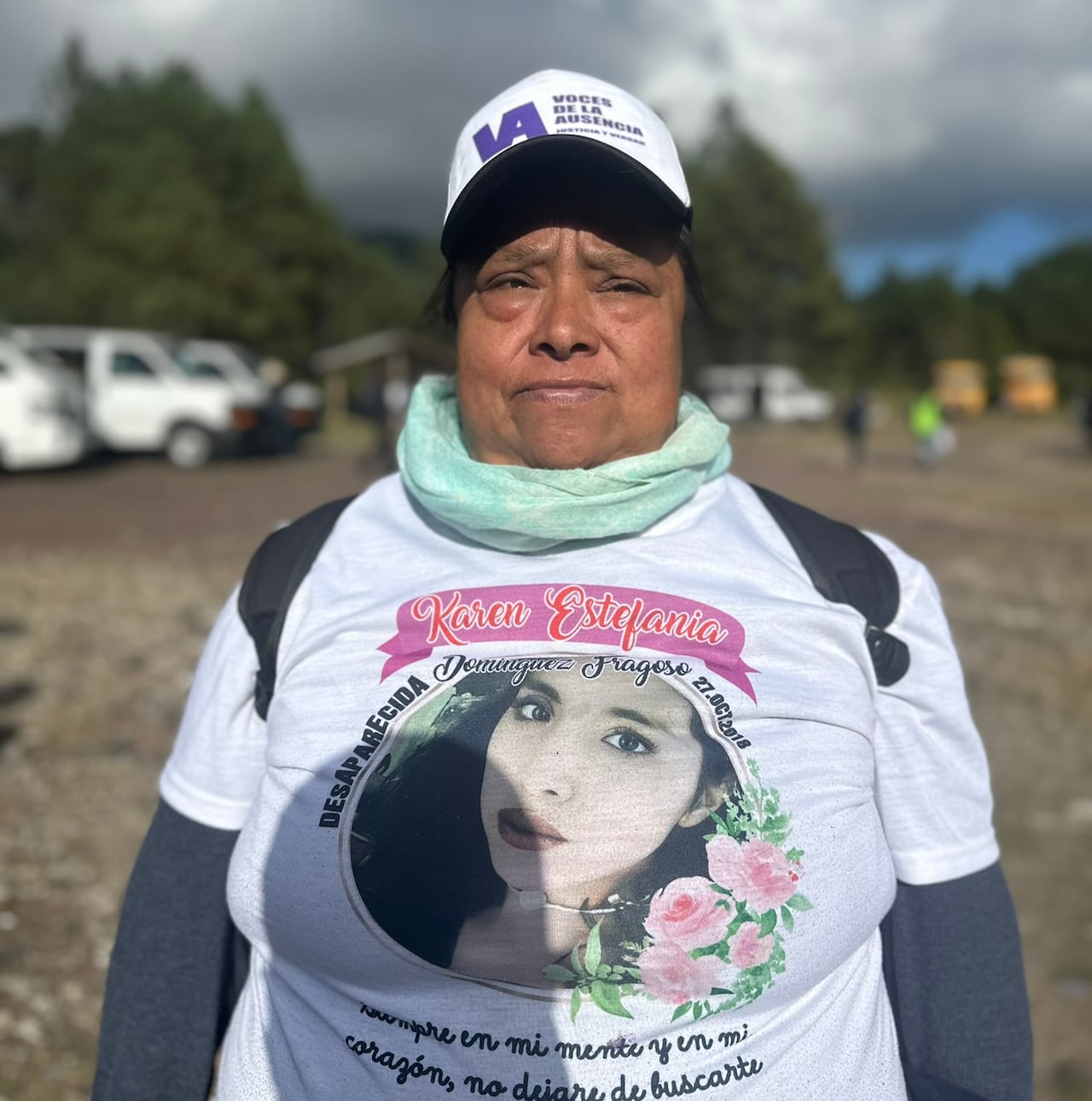 A woman with a white shirt with the photo of her daughter looks into the camera.