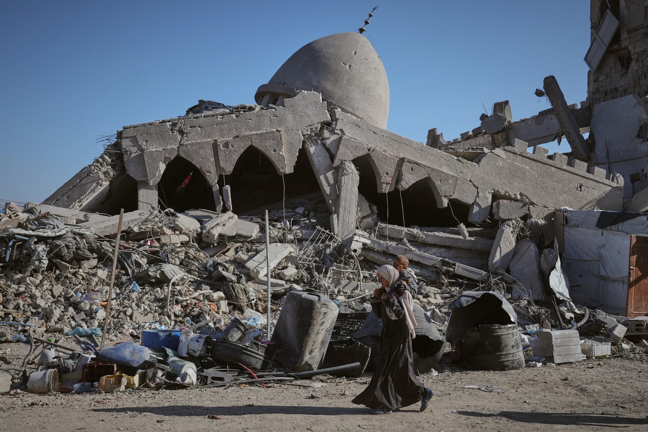 An adult carries a child on their shoulders as they walk past the destroyed building.