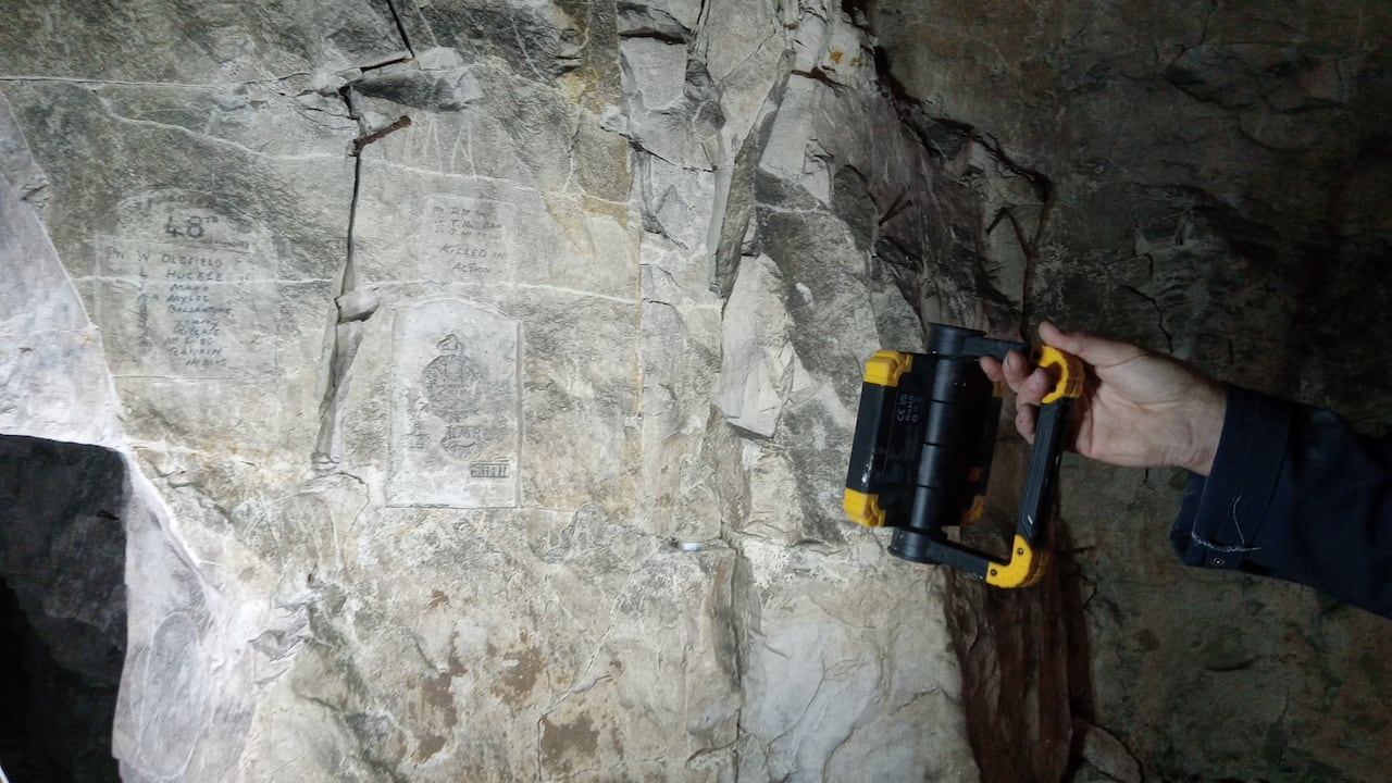A cave wall with a carving and a hand holding a flashlight to it.