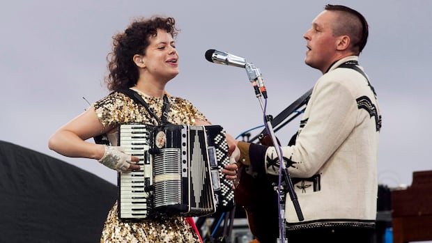 A woman holding an accordion stands beside a man holding a guitar