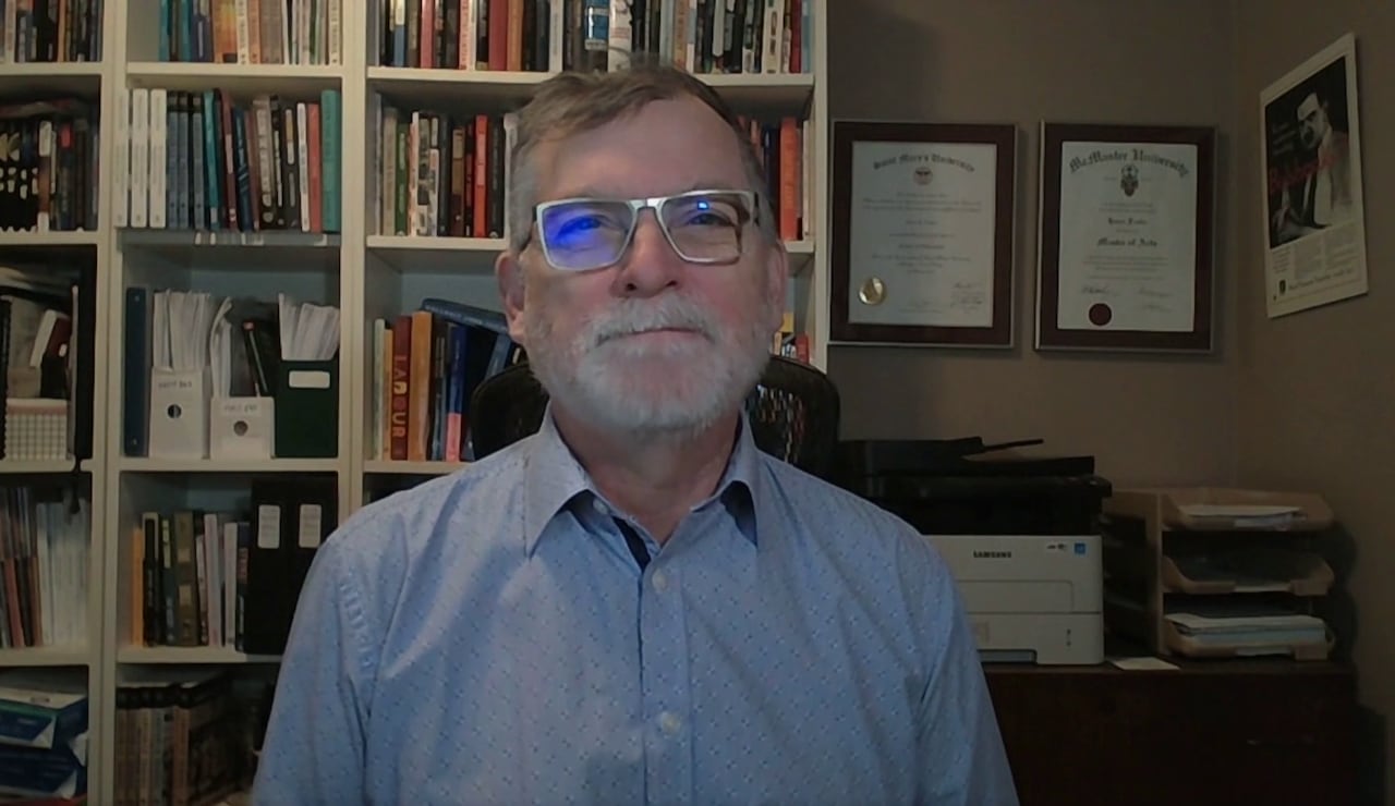 A man sits in front of a row of books.