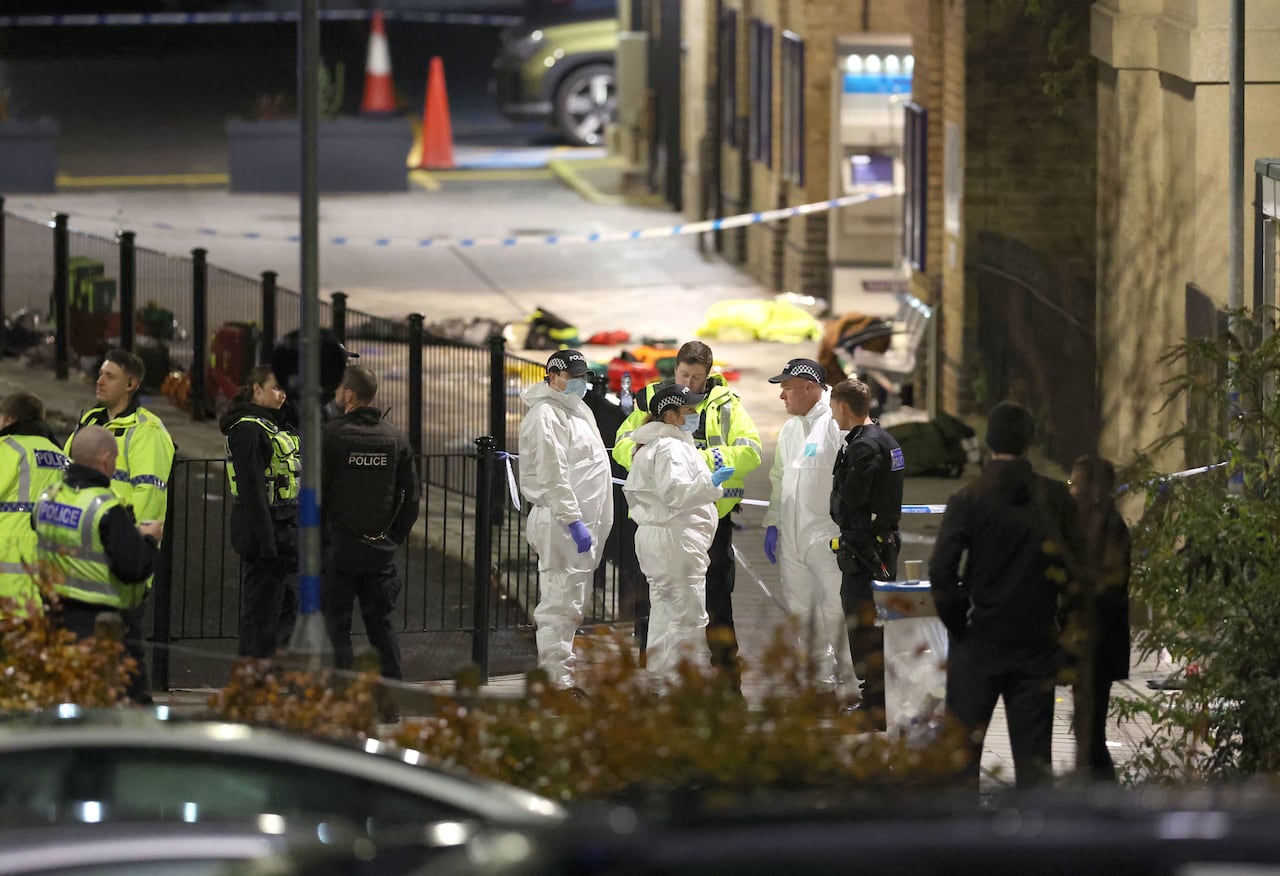 People in police uniforms and white plastic suits gather near a railway.