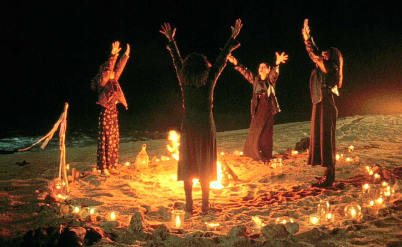 4 women standing around a circle of lit candles on the beach at night.