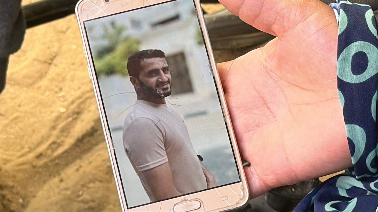 A hand holds a phone showing an image of a man smiling.
