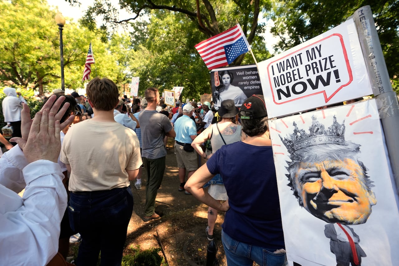 Several people were shown standing back and returned to the camera at an outdoor meeting. Signs shown again, including one of the man with a crown on his head.