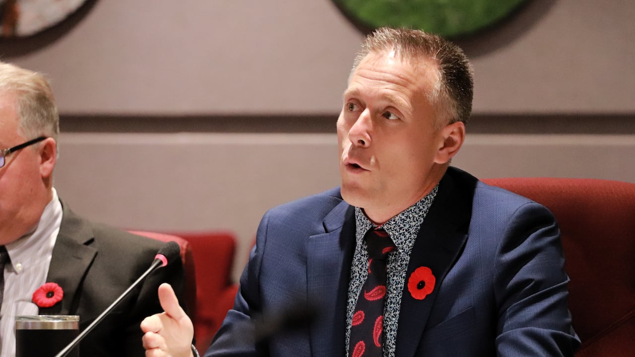 A man in a blue suit wearing a red poppy pin speaking into a microphone.