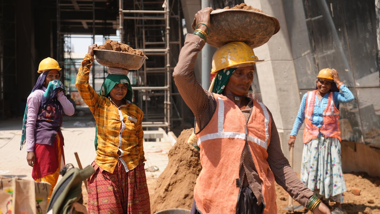 在建築工地附近,穿著色彩鮮豔的衣服、戴著安全帽的婦女們頭上頂著一桶桶泥土。