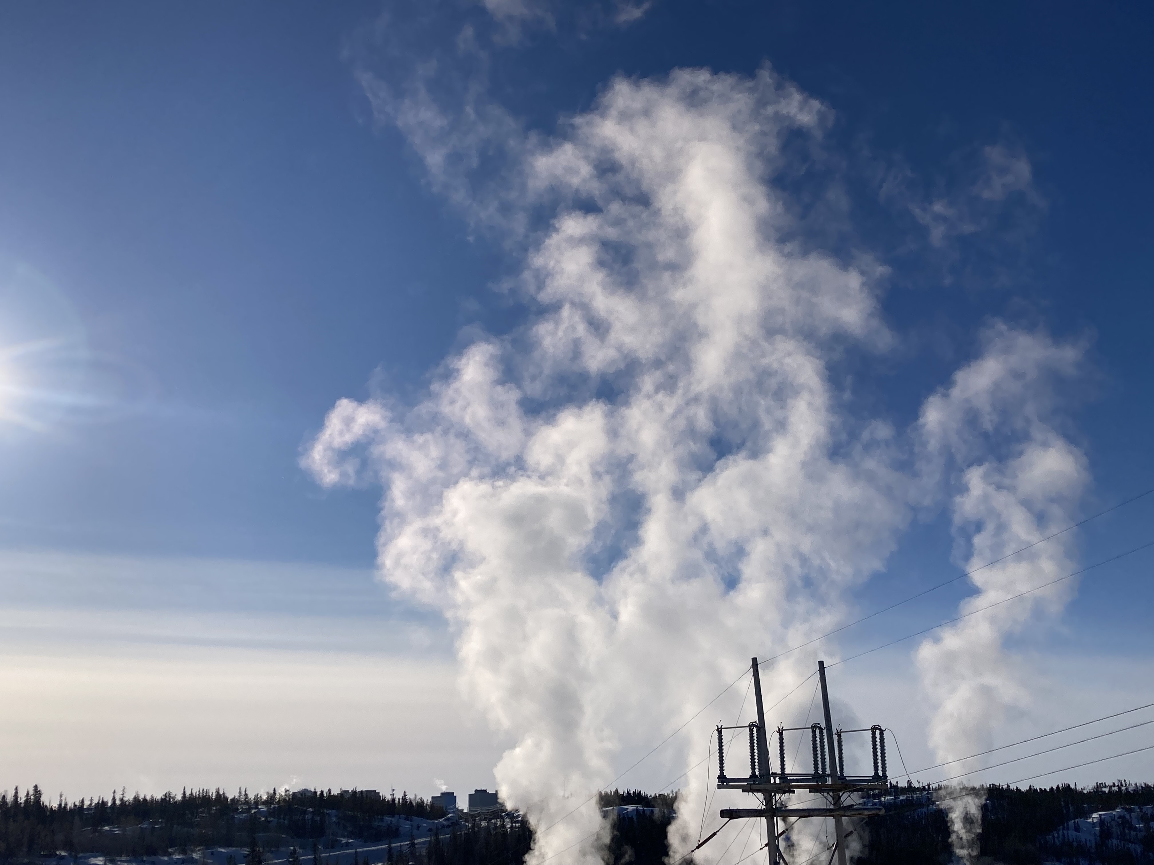 Fumes rise up from the Jackfish diesel generating plant in Yellowknife, N.W.T. in March 2024. Clouds appear to rise up against a clear, bright blue sky.
