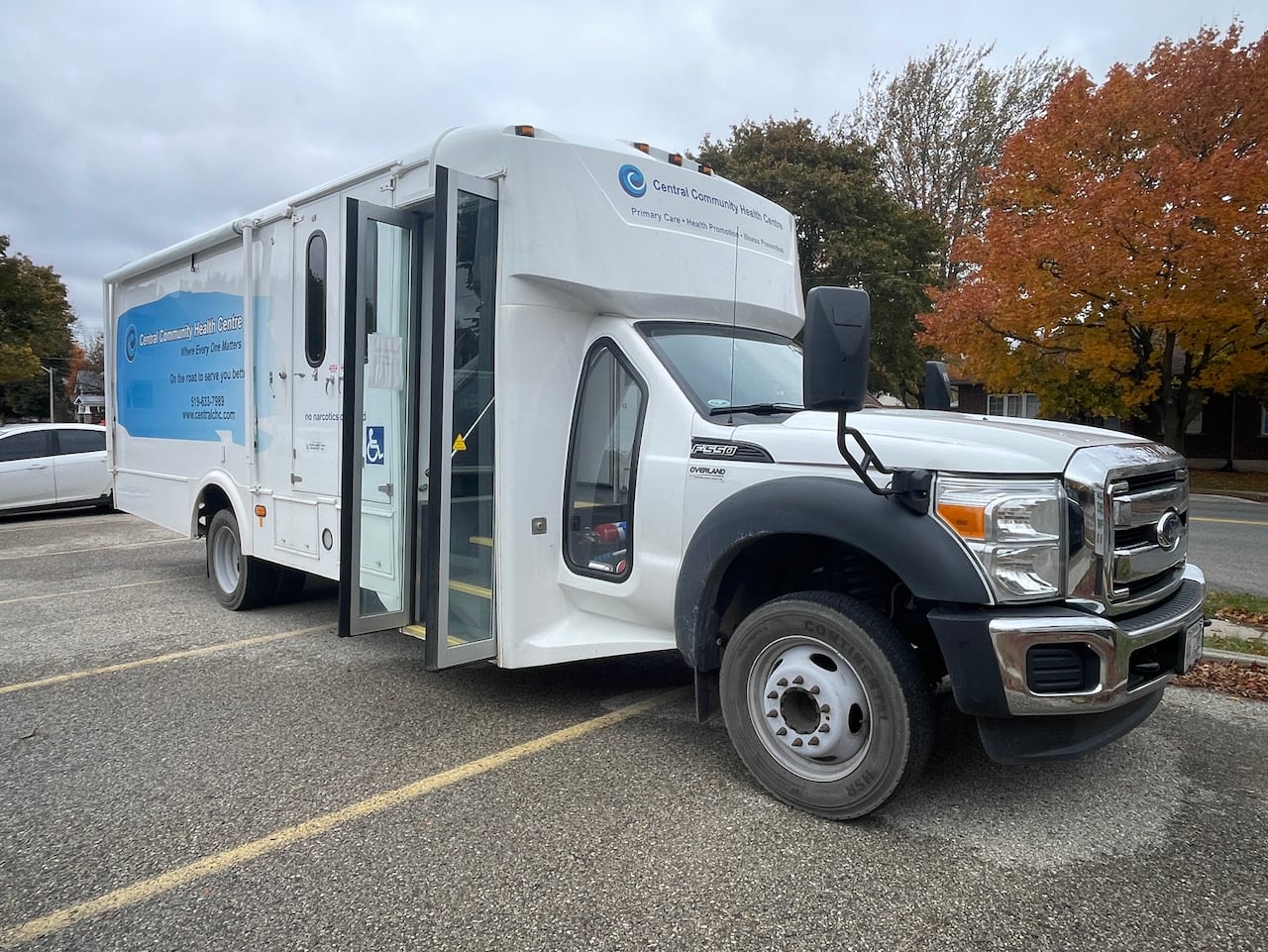 A mobile health unit on wheels parked in three spaces in a church parking lot.