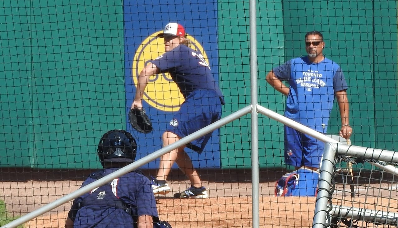 A pitching coach watches a player throw to a catcher.