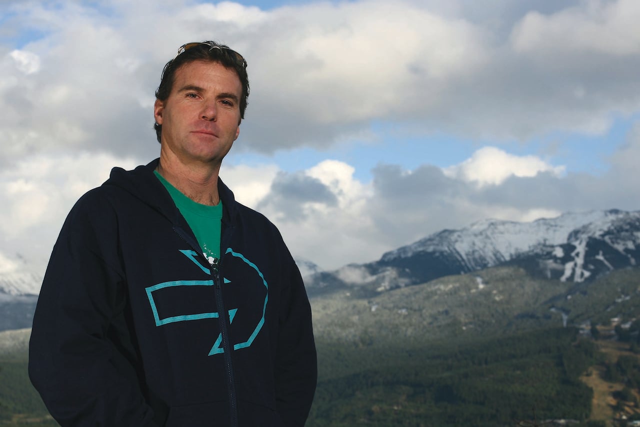 The man looks at the camera, with a mountain behind him.