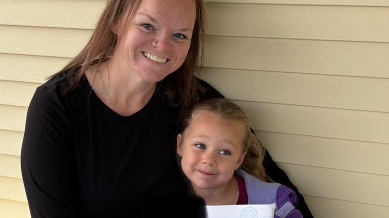 A woman smiling beside her daughter holding a sign declaring her first day of school