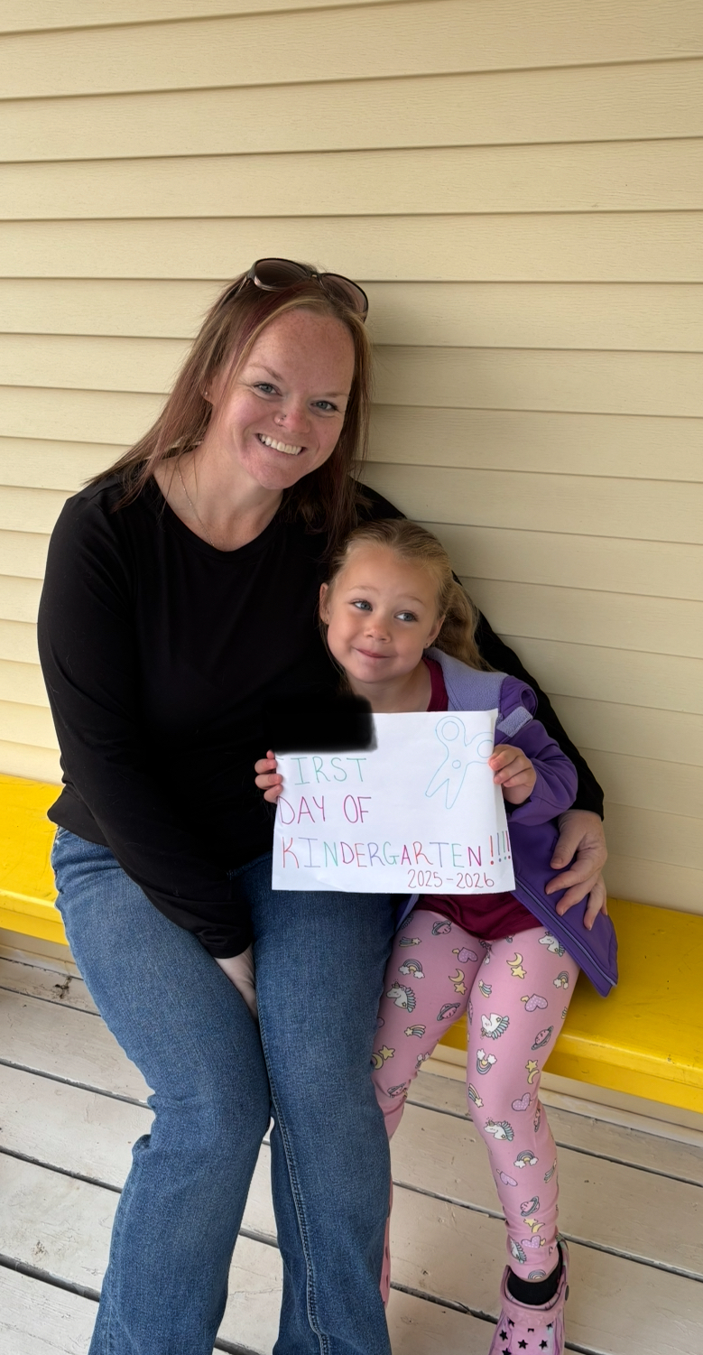 Joscelyn Croft worked hard last year to get the lunch program reinstated, only for her daughter and classmates to be excluded after 2 months A woman smiling beside her daughter holding a sign declaring her first day of school