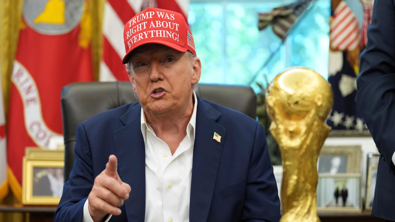 Man sitting at an office table wearing a hat that reads: Trump was right about everything.