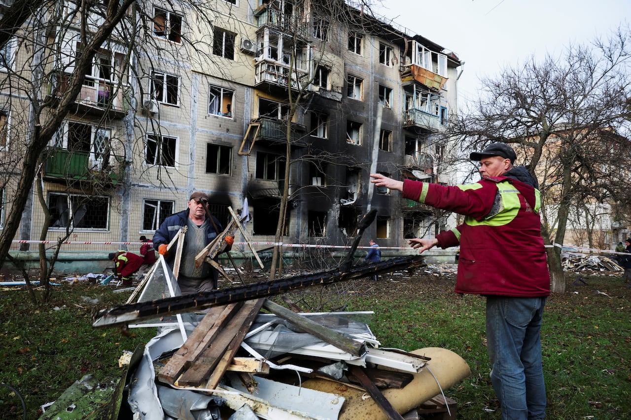 Two men clean up debris from the front yard of a burned and damaged apartment building.