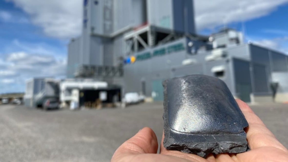 Brick of steel in a person's hand with factory in background
