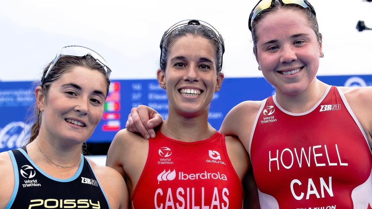 Three female triathletes smile as they stand side by side on the podium.