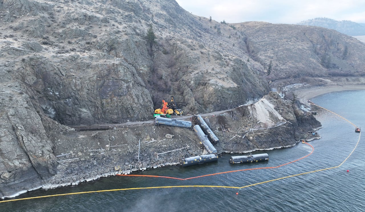 An oil boom and industrial equipment is seen along the side of a lake.