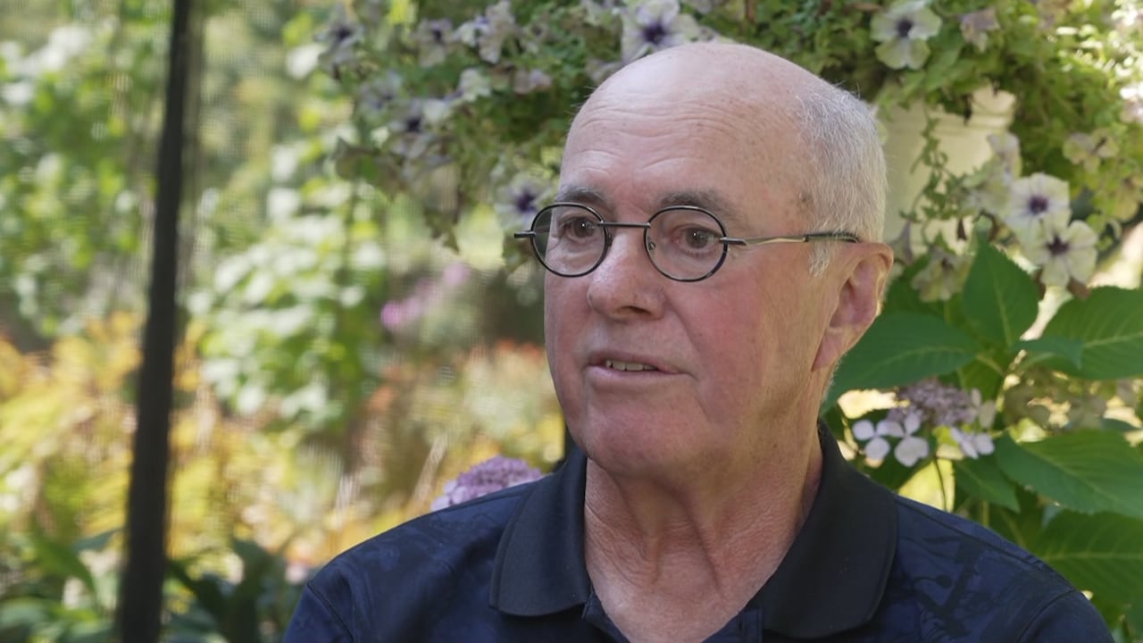 A man with glasses sitting outdoors in a backyard.