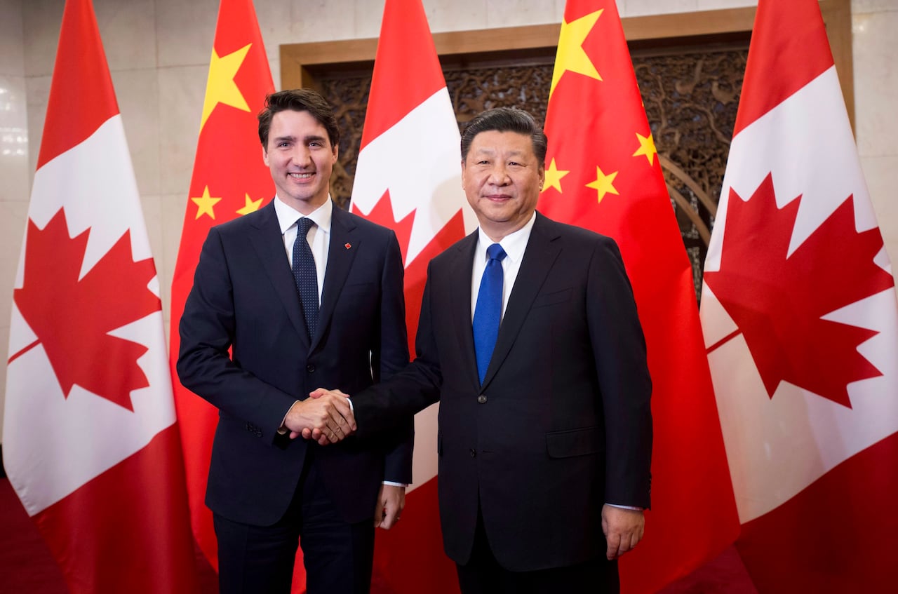 Dos hombres se dan la mano frente a banderas canadienses y chinas.