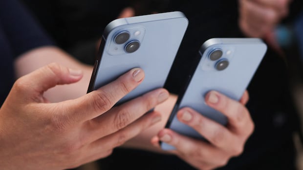 A guest holds the new iPhone 14 at an Apple event at their headquarters in Cupertino, California, U.S. September 7, 2022. A person holds two smart phones in their hands.