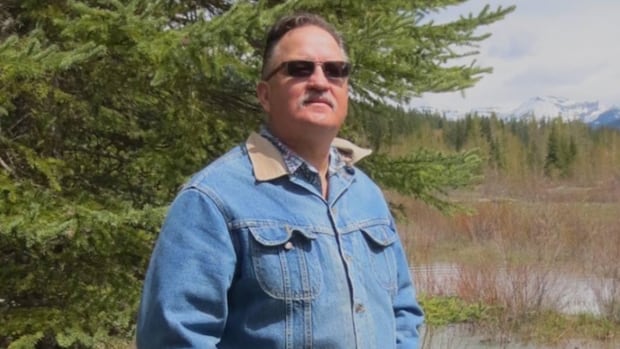 Joe Pendry, who was injured when he fought off a grizzly sow with two cubs, near Fort Steele, B.C., on Thursday, Oct. 2, 2025, is seen in this undated handout photo. Pendry continues to recover in Kelowna General Hospital after he shot the animal before fighting it off with his bare hands. A middle-aged white man with sunglasses wears a denim jacket and stands outside with a fir tree behind him.