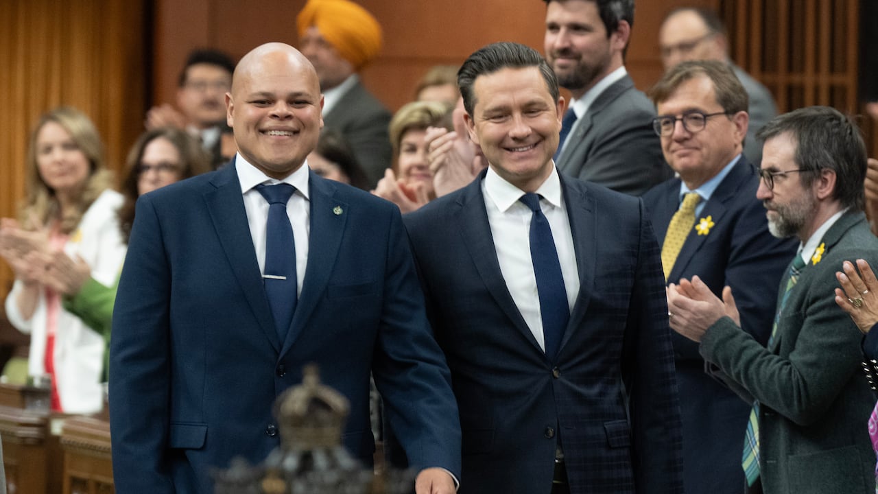 A bald man wearing a blue suit walks down the House of Commons with Pierre Poilievre.