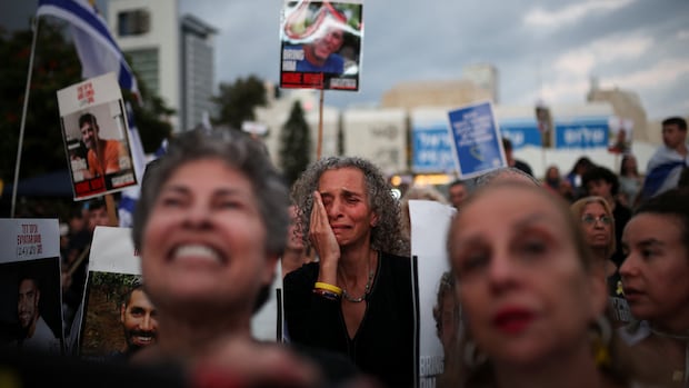 A women (centre) smiles as she wipes tears from her face as she stands among a crowd of people holding signs with photos of loved ones on them.