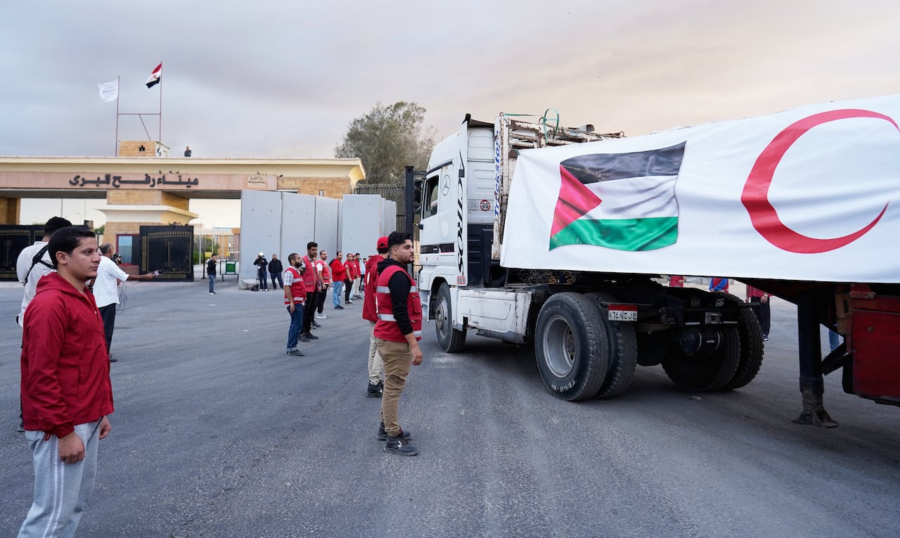 Men in red vests observe a large truck with a Palestinian flag on it.