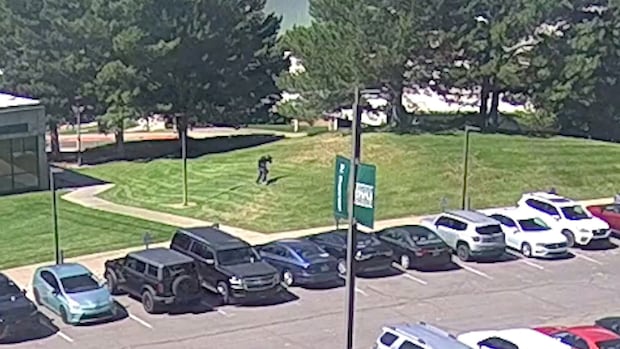 A video clip shot showing a man walking through the grass between a parking lot and a building