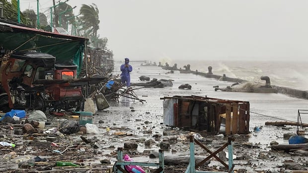 A man stands near debris on a waterfront road amid heavy rain.