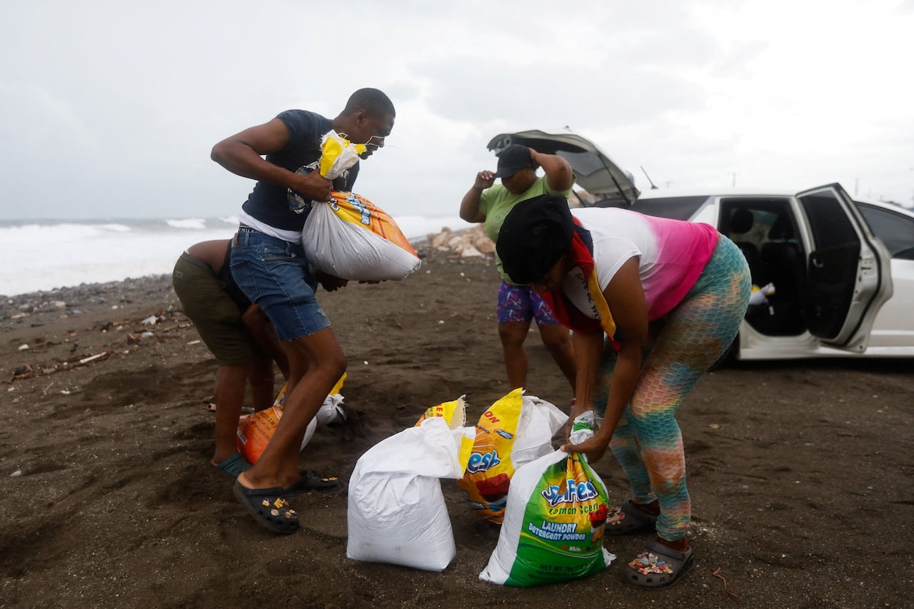 People load and carry bags of sand on a beach.