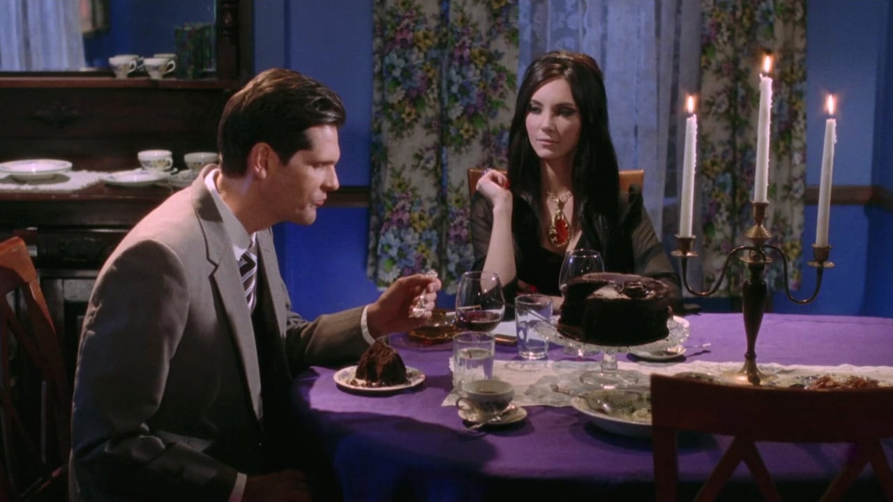 A man and woman sitting at a dinner table with a chocolate cake and candelabra on it.
