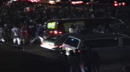 A screen capture from a grainy old video shows a crowd of people rocking a van back and forth.