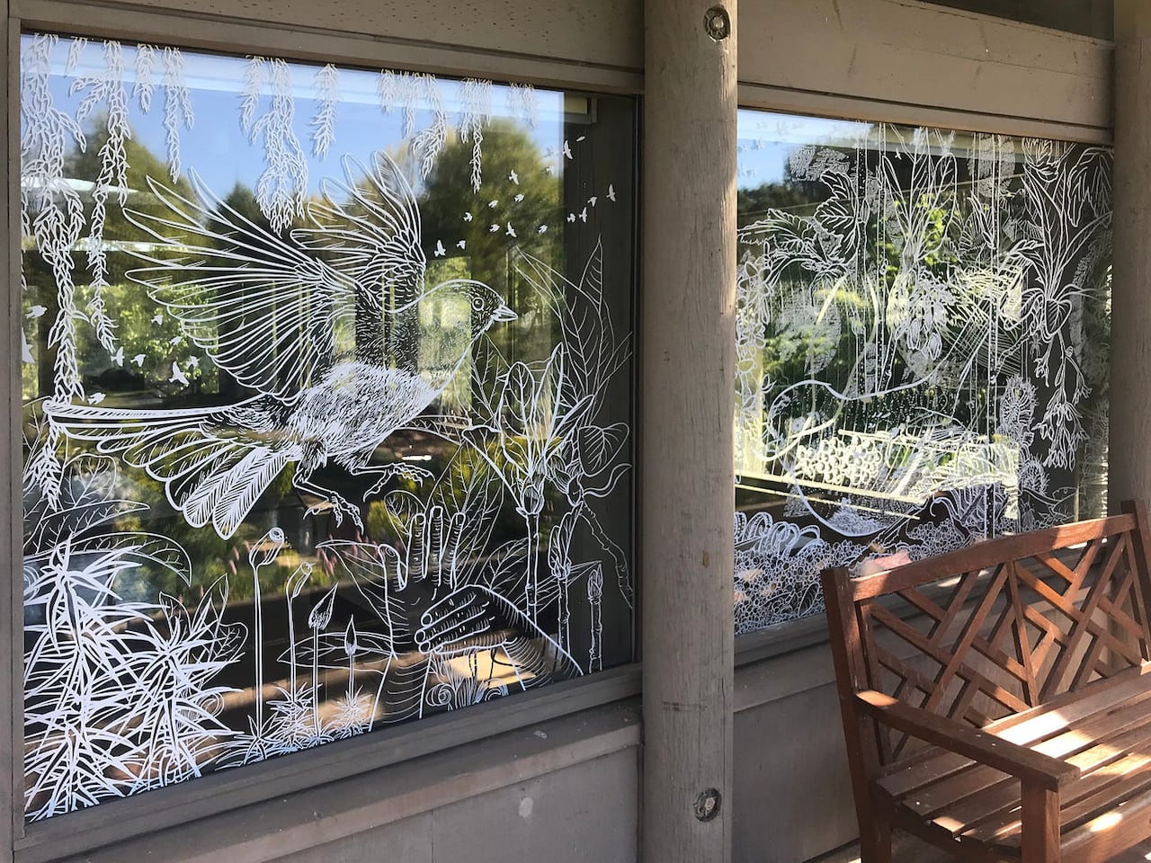 A window with an intricate design on it that depicts a bird in foliage in white opaque paint.