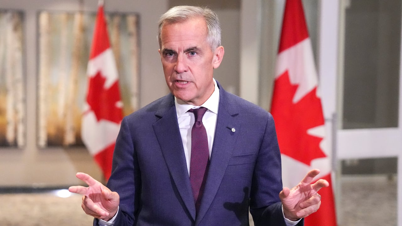 Prime Minister Carney standing in front of draped Canadian flags 