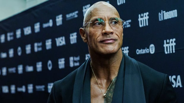 A man wearing glasses and a suit looks off camera in front of a TIFF red carpet.