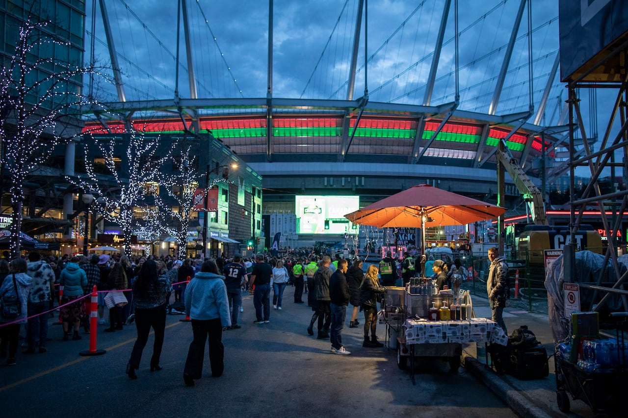 The large stadium is lit up in red and green, with fans milling around underneath and visiting the food stall.