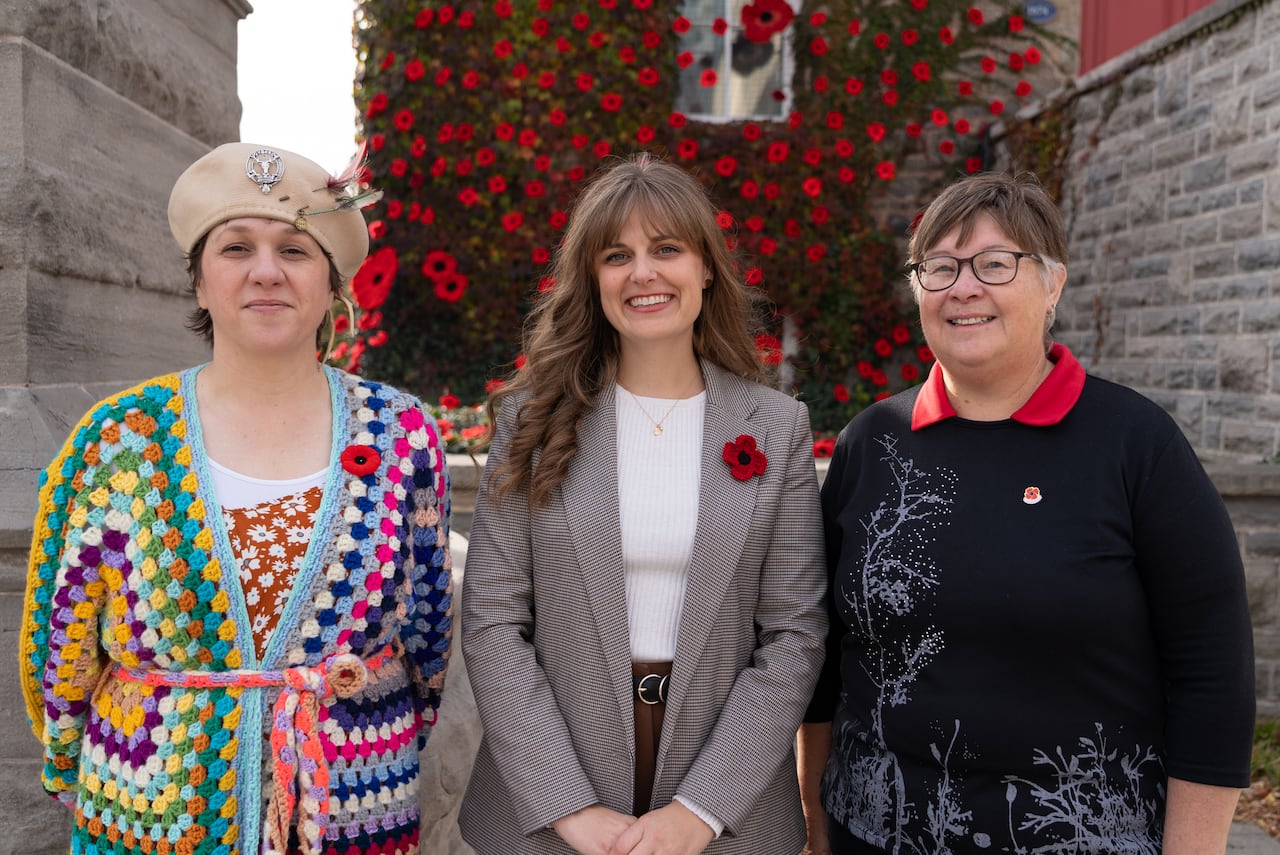 three women standing side by side in front of museum covered in poppies