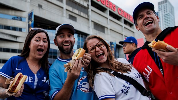People wearing Blue Jays shirts cheers in front of the Rogers Centre.
