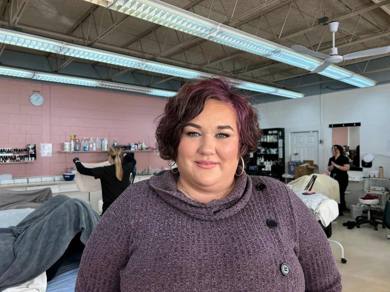 A pistillate   stands successful  an esthetician's studio. She is smiling astatine  the camera. 