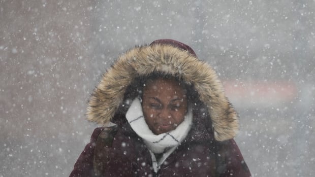 NEW YORK, NY - JANUARY 04: A woman walks through the snow toward the Atlantic Avenue-Barclays Center subway station during the morning commute, January 4, 2018 in the Brooklyn borough of New York City. As a major winter storm moves up the Northeast corridor, New York City is under a winter storm warning and forecasts are calling for six to eight inches of snow. (Photo by Drew Angerer/Getty Images) A woman squints as she walks through heavy snowfall. She wears a parka with a fur-lined hood, and a scarf.