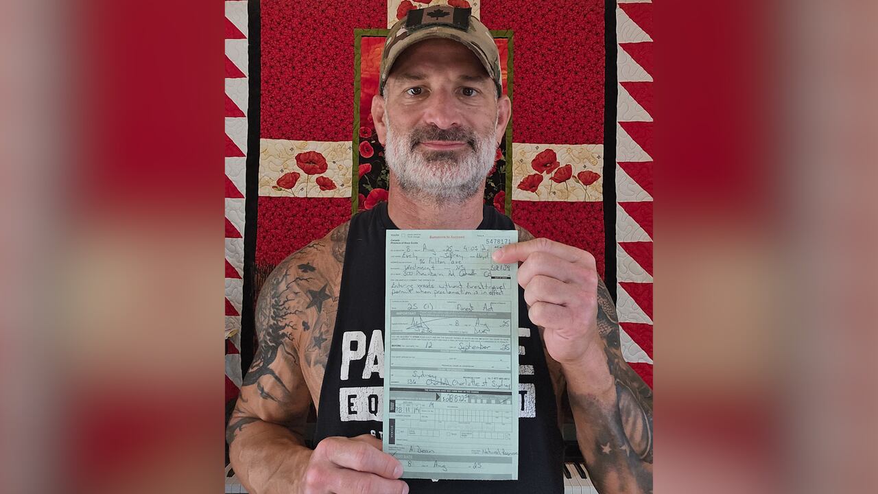 A man stands in front of a quilt on a wall and holds up a ticket.